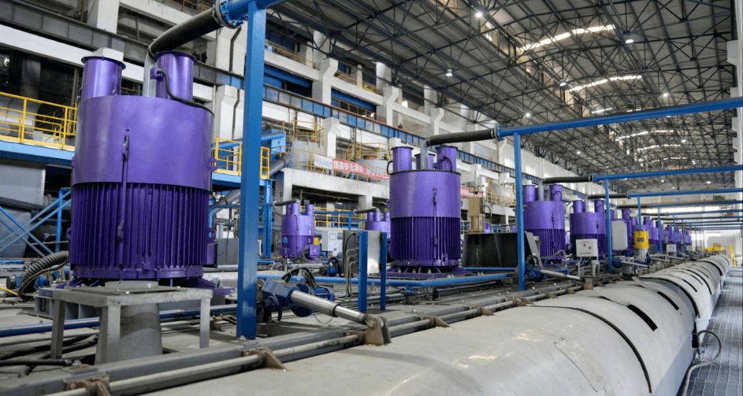 Row of large purple industrial motors and blue pipes inside a spacious manufacturing plant.