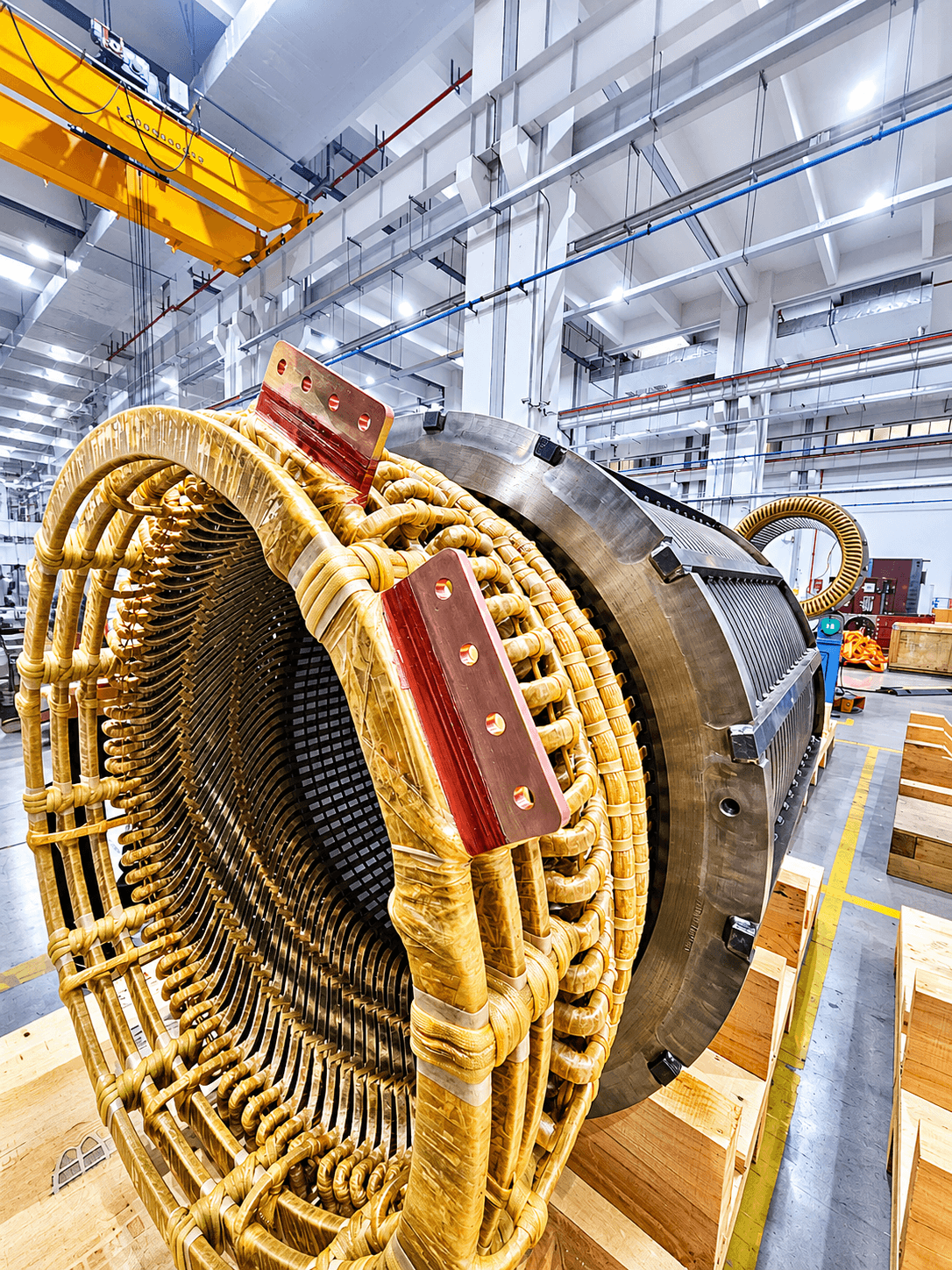 Large industrial motor stator with intricate yellow-wrapped copper windings in a factory setting.