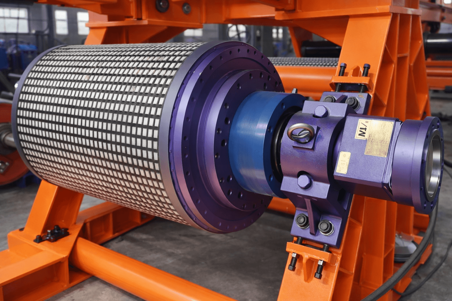 Heavy-duty industrial pulley with ceramic lagging and purple housing on an orange steel frame.